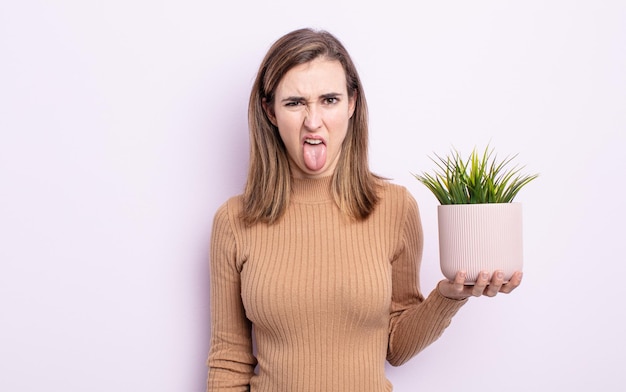 Mulher jovem e bonita se sentindo enojada e irritada e com a língua de fora. conceito de planta