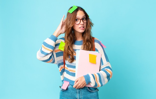 Mulher jovem e bonita se sentindo estressada, ansiosa ou com medo, com as mãos na cabeça com uma bolsa e segurando livros