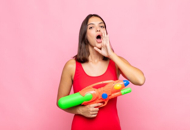 Mulher jovem e bonita se sentindo feliz, animada e positiva, dando um grande grito com as mãos perto da boca, gritando. conceito de verão