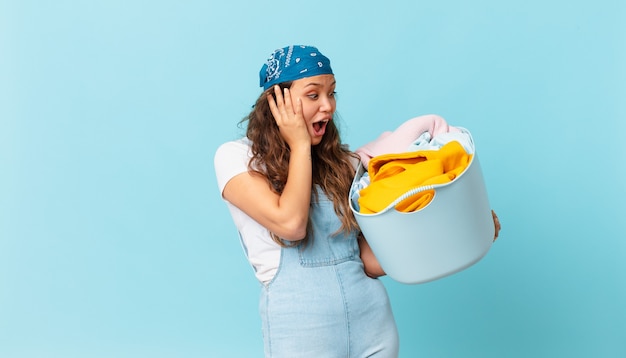 Mulher jovem e bonita se sentindo feliz, animada e surpresa, segurando uma cesta de roupas para lavar