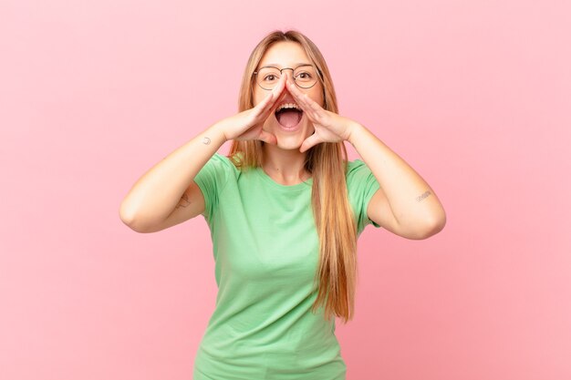 Mulher jovem e bonita se sentindo feliz, dando um grande grito com as mãos perto da boca