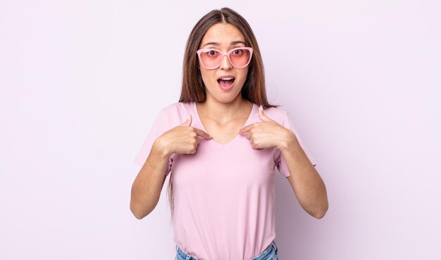 Mulher jovem e bonita se sentindo feliz e apontando para si mesma com um animado. conceito de óculos de sol rosa