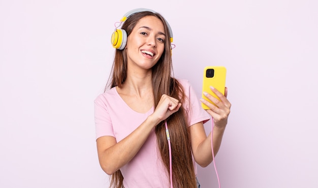 Mulher jovem e bonita se sentindo feliz e enfrentando um desafio ou comemorando. fones de ouvido e smartphone