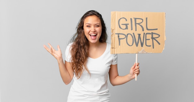 Mulher jovem e bonita se sentindo feliz e surpresa com algo inacreditável e segurando uma bandeira do poder feminino