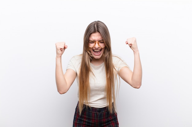 Mulher jovem e bonita se sentindo feliz, positiva e bem-sucedida, comemorando a vitória, conquistas ou boa sorte contra uma parede branca