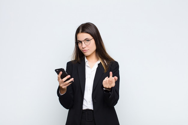 Mulher jovem e bonita se sentindo irritada, irritada, rebelde e agressiva, sacudindo o dedo médio, revidando com um telefone celular