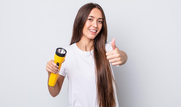 Mulher jovem e bonita se sentindo orgulhosa, sorrindo positivamente com o polegar para cima. conceito de lanterna