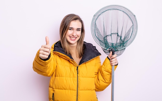 Mulher jovem e bonita se sentindo orgulhosa, sorrindo positivamente com o polegar para cima. conceito de pescador