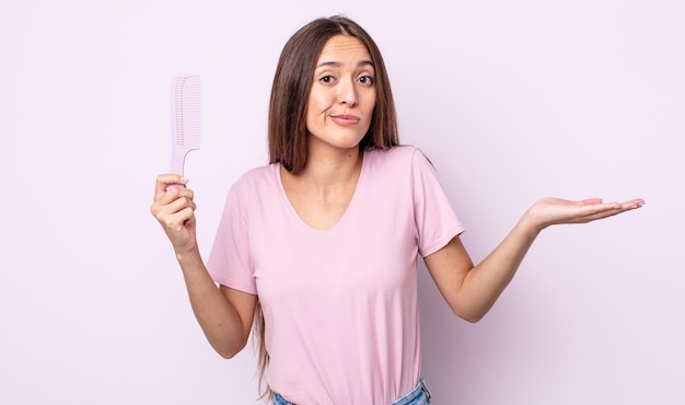 Mulher jovem e bonita se sentindo perplexa, confusa e em dúvida. conceito de pente de cabelo