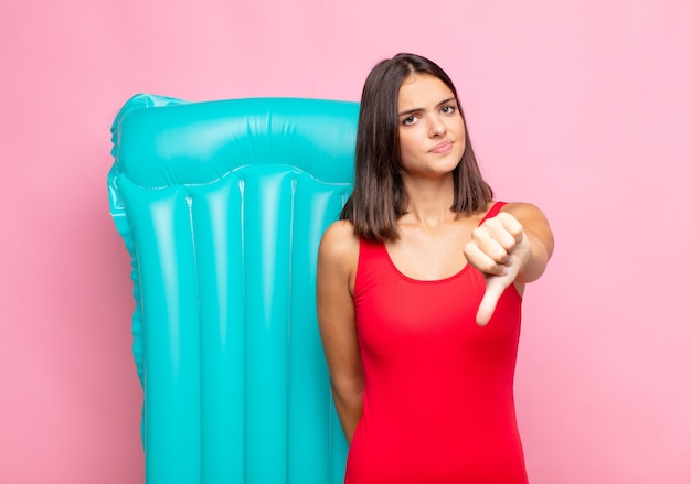 Mulher jovem e bonita se sentindo zangada, irritada, irritada, decepcionada ou descontente, mostrando o polegar para baixo com um olhar sério