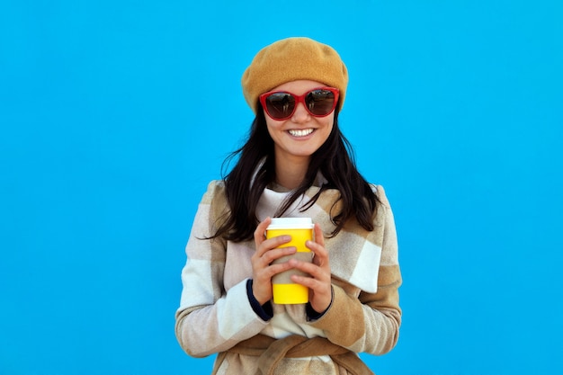 Mulher jovem e bonita segurando copo de papel com fundo azul de café quente