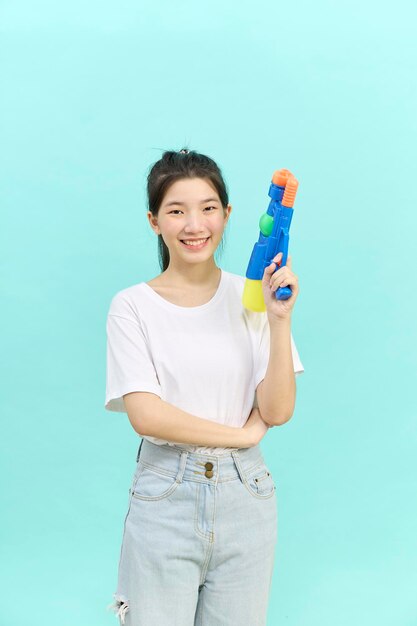 Mulher jovem e bonita segurando pistola de água no festival Songkran Tailândia isolado sobre fundo azul.