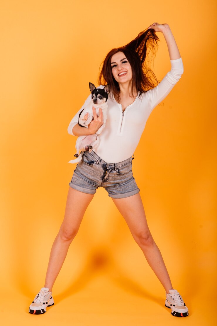 Foto mulher jovem e bonita segurando seu cachorro em um fundo amarelo.