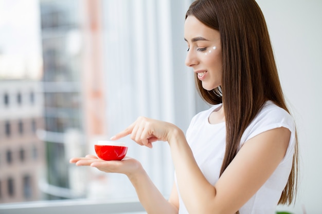 Mulher jovem e bonita segurando um creme cosmético hidratante