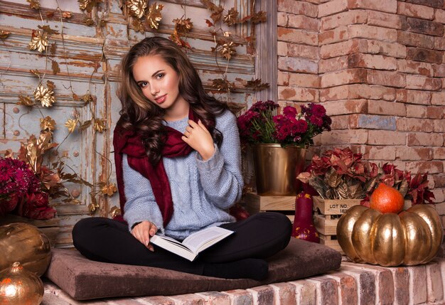 Mulher jovem e bonita senta-se com um livro no interior de outono.