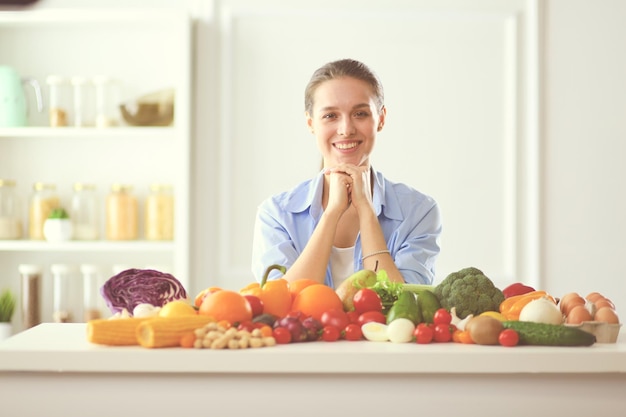 Mulher jovem e bonita sentada à mesa cheia de frutas e vegetais no interior de madeira