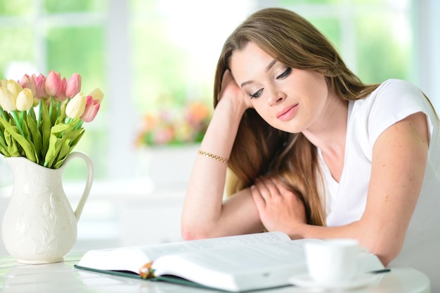 Mulher jovem e bonita sentada à mesa com livro aberto