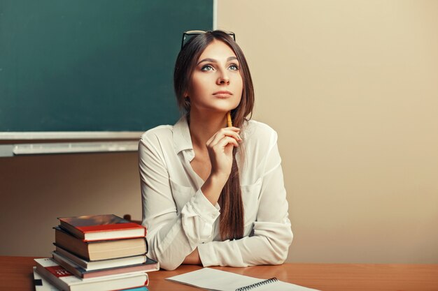 Mulher jovem e bonita sentada à mesa com livros e pensando