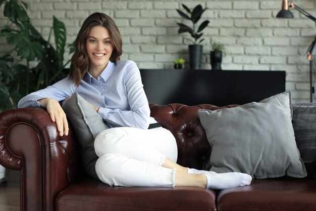 Foto mulher jovem e bonita sentada no sofá, dentro de casa.