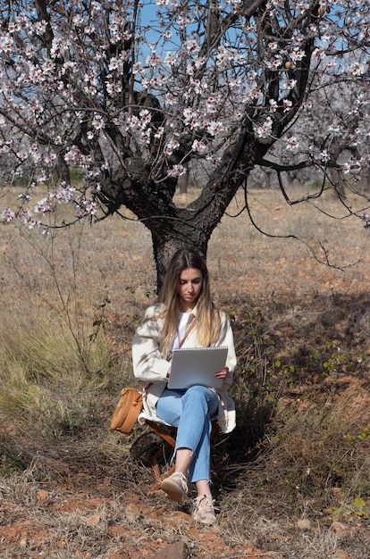 Mulher jovem e bonita sentada no tronco de uma árvore em flor enquanto desenha