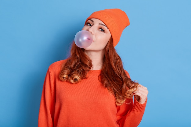 Foto mulher jovem e bonita soprando chiclete enquanto posa isolada sobre uma parede azul