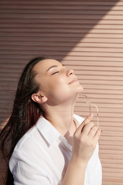 Mulher jovem e bonita sorridente com pele perfeita sem pêlos tirando os óculos de sol e aproveitando a luz do sol