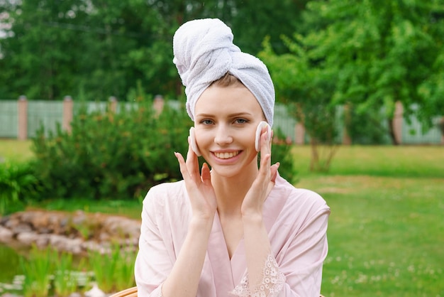 Mulher jovem e bonita sorridente com toalha na cabeça, segurando a almofada de algodão limpando o rosto