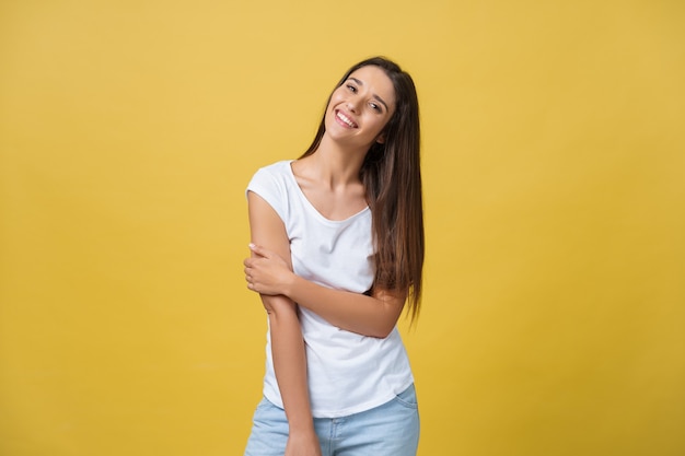 Mulher jovem e bonita sorridente em camisa branca, olhando para a câmera. Estúdio de comprimento de três quartos baleado em fundo amarelo.