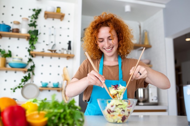 Foto mulher jovem e bonita sorridente na cozinha está preparando uma salada vegana em roupas casuais