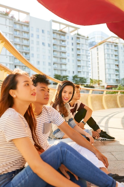 Mulher jovem e bonita sorridente, passando um tempo com suas melhores amigas sentadas na ponte e curtindo o bom tempo