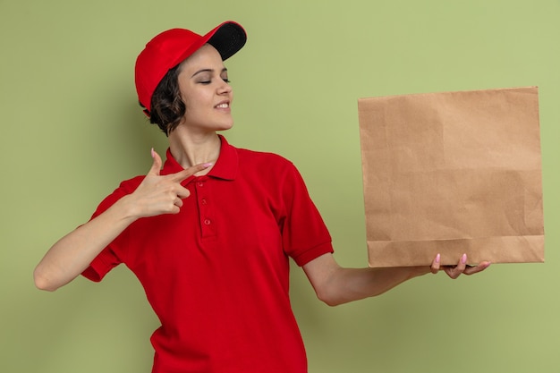 Foto mulher jovem e bonita sorridente, segurando e apontando para uma embalagem de comida de papel