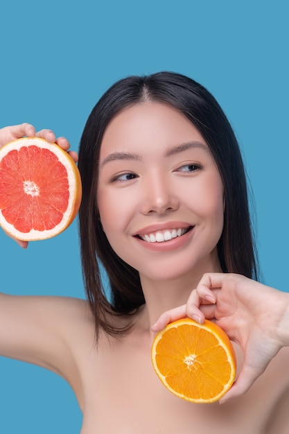 Mulher jovem e bonita sorridente segurando fatias de laranja e toranja