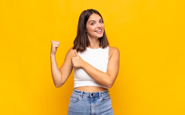 Mulher jovem e bonita sorrindo alegre e casualmente apontando para copiar o espaço ao lado, sentindo-se feliz e satisfeita