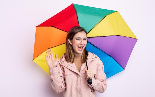 Mulher jovem e bonita sorrindo alegremente, acenando com a mão, dando as boas-vindas e cumprimentando você. conceito de guarda-chuva