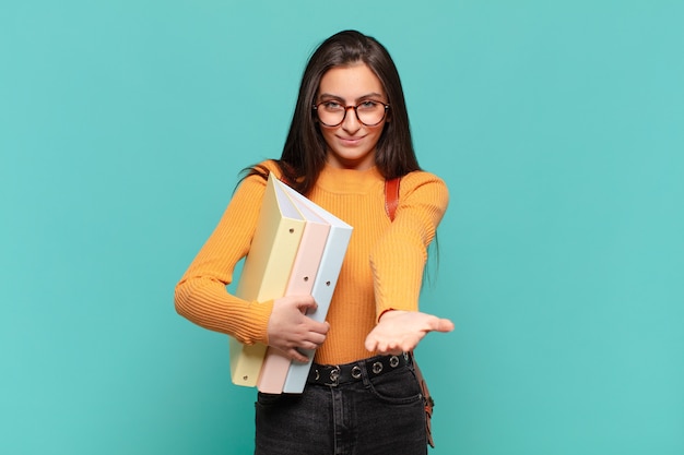 Mulher jovem e bonita sorrindo alegremente com olhar amigável, confiante e positivo, oferecendo e mostrando um objeto ou conceito. conceito de estudante