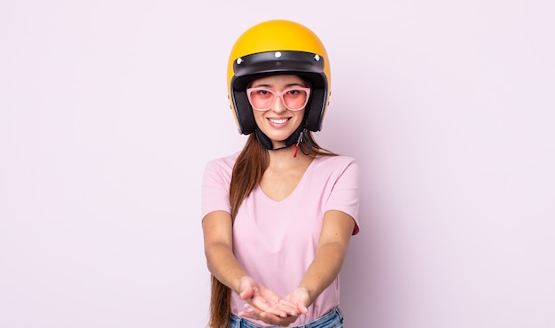 Mulher jovem e bonita sorrindo alegremente com simpáticos e oferecendo e mostrando um conceito. motociclista e capacete