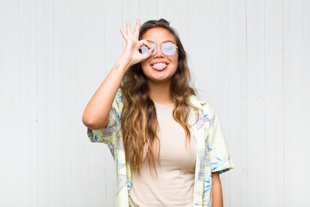 Mulher jovem e bonita sorrindo alegremente com uma cara engraçada, brincando e olhando pelo olho mágico, espionando segredos. conceito turístico