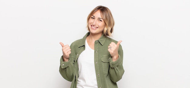 Mulher jovem e bonita sorrindo alegremente e parecendo feliz, sentindo-se despreocupada e positiva com os dois polegares para cima