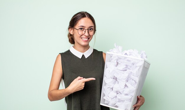 mulher jovem e bonita sorrindo alegremente, sentindo-se feliz e apontando para o lado. conceito de lixo de bolas de papel