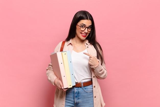 Mulher jovem e bonita sorrindo alegremente, sentindo-se feliz e apontando para o lado e para cima, mostrando o objeto no espaço da cópia