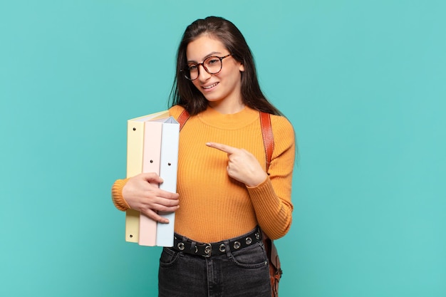 Mulher jovem e bonita sorrindo alegremente, sentindo-se feliz e apontando para os lados e para cima, mostrando o objeto no espaço da cópia. conceito de estudante