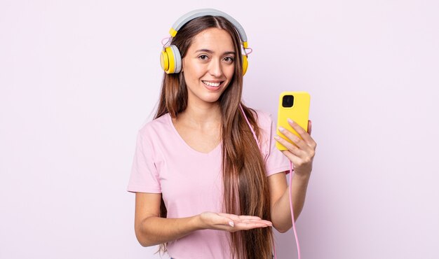 Mulher jovem e bonita sorrindo alegremente, sentindo-se feliz e mostrando um conceito. fones de ouvido e smartphone