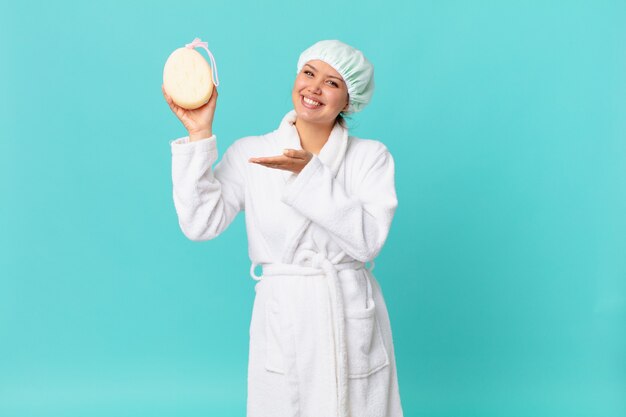 Mulher jovem e bonita sorrindo alegremente, sentindo-se feliz, mostrando um conceito e usando roupão de banho após o banho