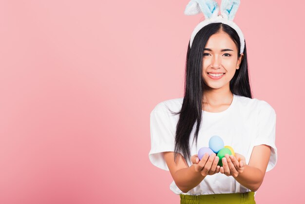 Mulher jovem e bonita sorrindo com orelhas de coelho e segurando ovos de Páscoa coloridos presentes nas mãos