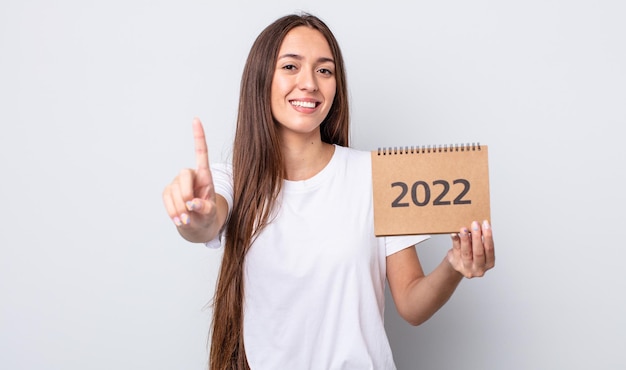 Mulher jovem e bonita sorrindo com orgulho e confiança, fazendo o número um. Conceito de planejador 2022