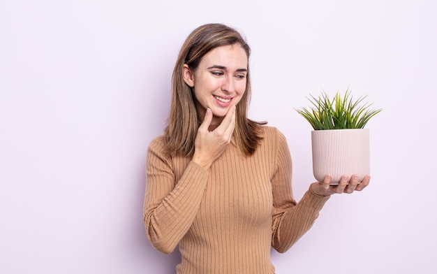 Mulher jovem e bonita sorrindo com uma expressão feliz e confiante com a mão no queixo. conceito de planta