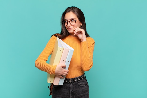 Mulher jovem e bonita sorrindo com uma expressão feliz e confiante com a mão no queixo, pensando e olhando para o lado. conceito de estudante