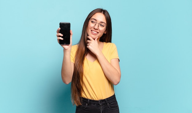 Mulher jovem e bonita sorrindo com uma expressão feliz e confiante com a mão no queixo, pensando e olhando para o lado