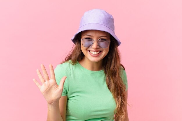 Mulher jovem e bonita sorrindo e parecendo amigável, mostrando o número cinco. conceito de verão