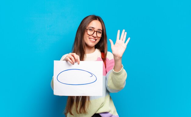 Mulher jovem e bonita sorrindo e parecendo amigável, mostrando o número cinco ou quinto com a mão para a frente, em contagem regressiva